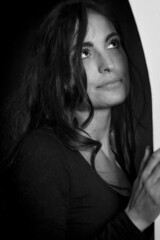 Black and white portrait of a beautiful long haired young woman leaning against an arched wall looking up