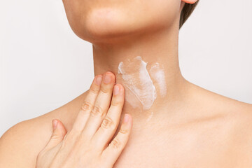 Close-up of a young woman's neck. The girl applies a cream to moisturize the neck skin isolated on a white background. Wrinkles, lines age-related changes, anti-aging procedures, treatment. Skin care