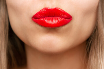 Cropped shot of a young beautiful caucasian blonde woman blowing a kiss with her lips with glossy red color lipstick. Beauty and fashion concept