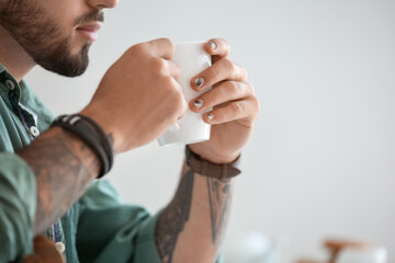 Man with stylish manicure holding cup on light background, closeup