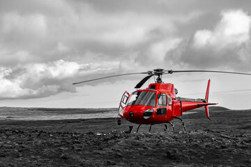 Fototapeta na wymiar Red Helicopter landed near Thrihnukagigur Volcano in Iceland on a Lava field near Bláfjöll Country Park and Reykjavik for tourists. Modern aviation in contrast with archaic colorless scenery.