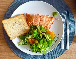 lunch of baked fish and salad with bread on a white plate