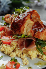 Delicious croissant sandwich with ham, cheese and scrambled eggs on plate served