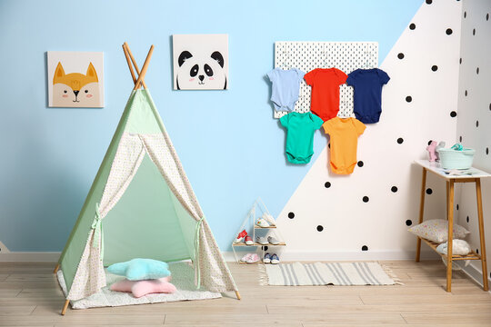 Interior of stylish children's room with pegboard, baby bodysuits and play tent