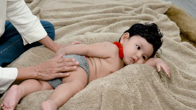 4K 50fps, A cute baby boy is sleeping on a soft brown bed, with his mother's hand stroking his bottom to lull the boy.Family and Healthy.