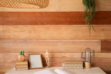 Modern workplace with books, frame and decor near wooden wall