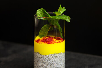 Chia pudding with mango puree in transparent glass isolated on black background.