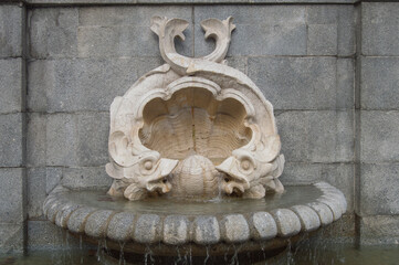 historic stone fountain with two fish and a shell in a street in Madrid. Spain