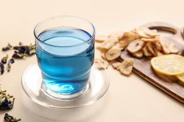 Cup of blue tea and dried butterfly pea flowers on color background, closeup