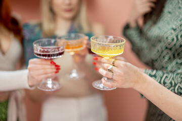 Women clinking glasses with alcohol drinks, celebrating women's day indoors. Close-up on glasses with colorful drinks