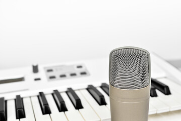 Professional studio microphone for voice and music recording against blurred synthesizer keyboard background with copy space.