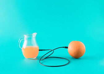 Orange and orange juice in a jug are connected by a cable. Minimal layout fruit concept.