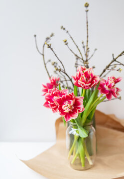 A beautiful spring bouquet of tulips stands in a vase along with spring branches. Surprise concept, birthday. Vertical photo, place for an inscription.