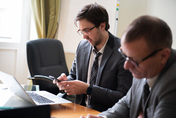 Young businessman using phone during roundtable business meeting