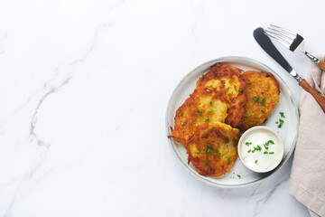 Potato pancakes. Fried homemade potato pancakes or latkes with cream and green onions in rustic plate on white marble table background. Rustic style. Healthy food. Top view.