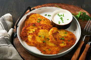 Potato pancakes. Fried homemade potato pancakes or latkes with cream and green onions in rustic plate on old wooden black table background. Rustic style. Healthy food. Top view.