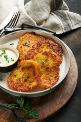 Potato pancakes. Fried homemade potato pancakes or latkes with cream and green onions in rustic plate on old wooden black table background. Rustic style. Healthy food. Top view.