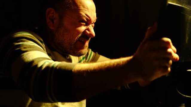 The man freaks out at the computer. Work at night at home. An unshaven middle-aged man shakes the monitor aggressively. Burnout, fatigue, irritability concept.