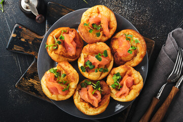 Yorkshire pudding. Traditional English Yorkshire pudding with salmon and radish microgreens side dish on dark grey plate and dark background table. Top view.
