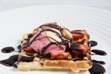 Delicious wafle with strawberries and chocolate syrup on a white dish