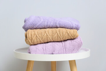 Stack of knitted sweaters on table near light wall