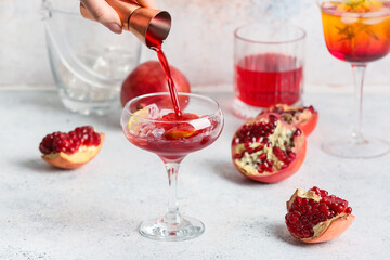 Woman adding pomegranate syrup in glass on light background