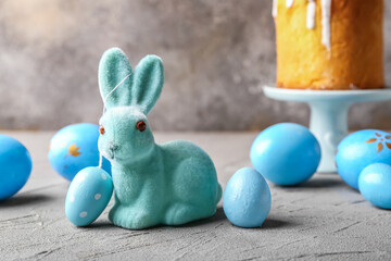 Cute Easter bunny with cake and painted eggs on color background