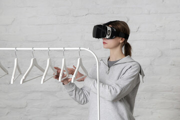 Portrait of woman with VR glasses choosing outfit from clothes hanger. Virtual reality experience and future technology concept. 