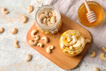 Obraz na płótnie Canvas Board with jars of sweet cashew nuts in honey on grunge background
