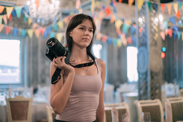 Girl photographer with a camera at work on the set in the banquet hall. A young beautiful woman - a...