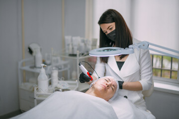 Cosmetologist and dermatologist makes injections with a mesotherapy apparatus to a lying woman...