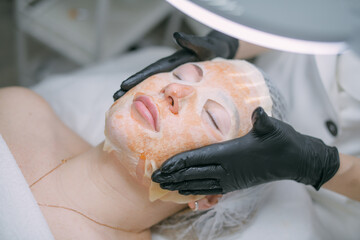 Cosmetologist and dermatologist makes a moisturizing, rejuvenating woman lying patient in a beauty salon.