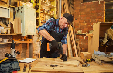 Portrait of a senior carpenter with drilling instrument working in the carpentry workshop to make a...