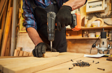 Senior carpenter with drilling instrument working in the carpentry workshop to make a piece of...