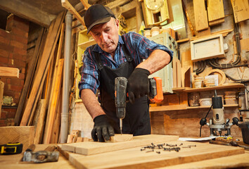 Portrait of a senior carpenter with drilling instrument working in the carpentry workshop to make a...