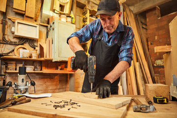 Portrait of a senior carpenter with drilling instrument working in the carpentry workshop to make a piece of furniture
