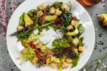 Avocado salad with baby spinach and pomegranate on a black plate on a slate,stone or concrete background.Top view with copy space