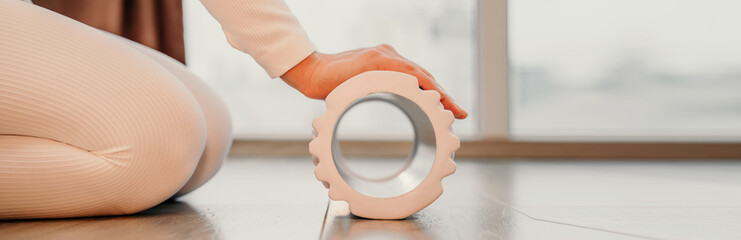 Adult athletic woman, in white bodysuit, performing fascia exercises on the floor - caucasian woman using a massage foam roller - a tool to relieve tension in the back and relieve muscle pain - the