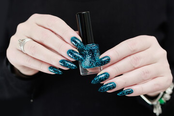 Woman hand with long nails and teal blue green manicure with bottles of nail polish