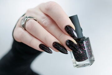 Female hands with long nails and total black manicure holding a bottle of nail polish