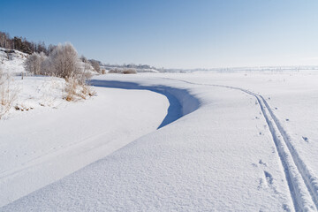 Obraz premium Ski tracks pass next to the frozen riverbed. Winter beautiful landscape. Large snowdrifts, a ski trip in the park.