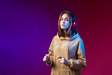 Fototapeta na wymiar Young beautiful fashionable hipster girl dressed in a hoodie listening to music in red headphones in a studio red dramatic background