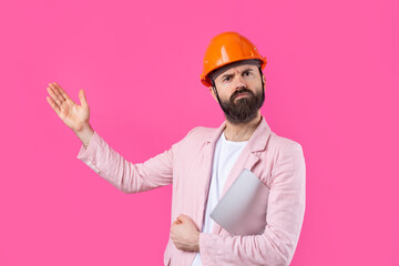 Portrait of young construction engineer wear orange hard hat, in a pink jacket standing on red studio background. A man with a tablet in his hands.