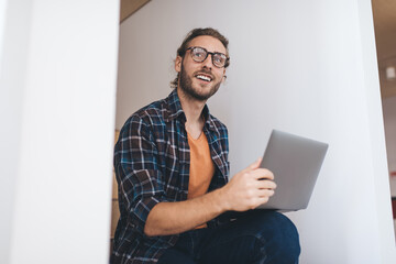 Skilled digital blogger in classic eyewear for vision correction looking away while working remotely, Caucasian software developer in eyewear with modern laptop computer doing distance job indoors