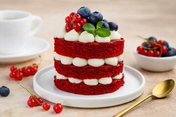 Mini red velvet cake decorated with berries and mint. Portion cake on a white plate with a cup of...