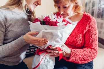 Daughter giving her mother bouquet of flowers at home as Mother's day present. Senior woman...