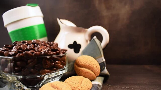 Coffee beans, cookies, milk jug and plastic thermos for hot drinks left by a hand on black table 