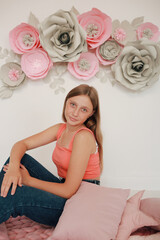 Obraz na płótnie Canvas Beautiful teen girl in jeans and pink top. Photo shoot in pink paper flowers and pink pillow