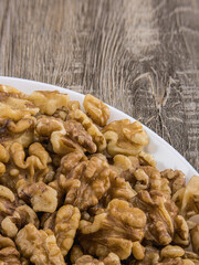 Peeled walnuts on white ceramic bowl on wooden textured