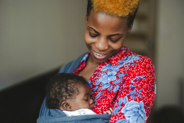 Mother with newborn in baby sling carrier at home
